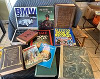 Group photo of all 12 vintage hardcover books laid out on a chair and table. Titles include BMW Cars, Time World Atlas, Guinness Book of Records 1981, Heroes of the Sea, Mark Twain, Webster Encyclopedia, Ripley's Believe It or Not and others.