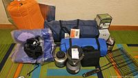 Photo showing all camping gear including orange packed tent, blue rolled item, gas lanterns, boxed gas burners, and air pumps.