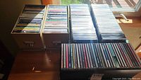 Several cardboard boxes and a rack filled with stacked CD jewel cases on a tabletop