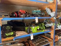 Shelf overview showing EGO batteries, charger, attachments and Greenworks trimmer head