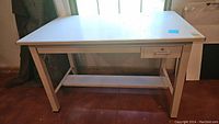 Full side view of the white drafting table showing front drawers and rectangular metal legs.