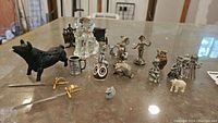 Various small figurines made from glass, metal, and plastic including animals, human-like figures, and small objects arranged on a glass surface
