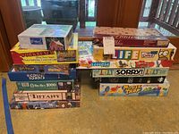 Photo of stacked board games and puzzles including Simpsons Life, Scrabble, Life, Sorry, Mouse Trap, Ricochet Robots, Workbench Puzzle, Big Ben and Tiffany puzzles.