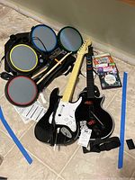 Overall lot showing drum pads, guitars, drumsticks, and game discs