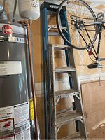 Photo showing the ladders leaning against a wall next to a water heater and a hanging bicycle, details the height and general construction of the ladders.