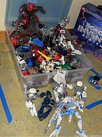 Plastic bin filled with assorted Bionicle pieces and assembled figures around it