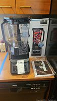 Ninja BN700 blender unit on kitchen counter with original box in background and user manual in plastic sleeve next to it.