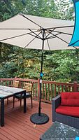Full view of outdoor beige umbrella set up on deck with metal stand holding it upright, surrounded by outdoor furniture.