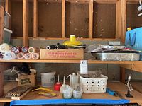 Shelf with assorted paint supplies including rollers in plastic packaging, paint trays, brushes, and plastic bottles