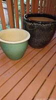 Photo of two ceramic pots: larger dark speckled pot and smaller green pot with beige rim, placed on wooden surface.