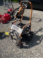 Front view of the Rigid pressure washer showing the orange metal frame, coiled hose, and large wheels.