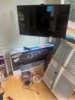 Samsung 40-inch UHD TV mounted on wall above original box, included remote visible on top of box, cables and accessory devices on floor next to box.