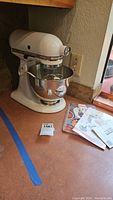 White KitchenAid Ultra Power stand mixer with stainless steel bowl on countertop. Original booklets and manuals placed next to mixer.