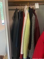 View of 8 assorted women's jackets hanging on wooden hangers in a closet rod, colors include gray, blue, white, red, lime green, herringbone black and white pattern.