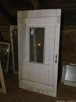 Front view of an antique white wooden door with a rectangular glass window and metal latch, showing aged wear and broken glass in the corner.