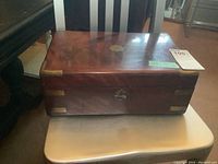 Frontal view of the closed antique solid wood writing box placed on a chair, showing the polished wooden surface and lock with no key.