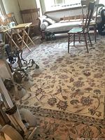 Full view of the cream floral wool area rug in living room with visible furniture and overall wear.