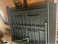 Black metal headboard and footboard for a bed with spindle design, stacked against wall in barn/dirt floor surroundings.