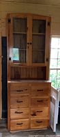 Full view of knotty pine buffet hutch with glass door upper cabinet and multiple drawers below.