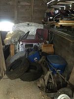 Overview of white body panels (doors, hood) leaning against barn wall with blue storage bins and chassis parts in front