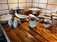 Christmas patterned dinnerware including plates, bowls, mugs, serving pieces and shakers arranged on countertop.