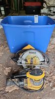Dewalt circular saw placed in front of the blue plastic tote on dirt floor, showing saw body, blade and cord