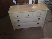 Front view of wooden dresser showing 3 drawers with different knob types and peeling paint on top and drawer fronts.