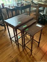 Set of three wooden nesting tables stacked together showing uneven surfaces and visible wear.