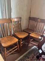 Four wooden dining chairs grouped together, showing carved decorative detail on the backrests and turned legs.