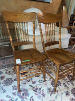 Two wooden chairs with carved details and spindle backrests placed on a patterned rug in a room with a white couch in the background.
