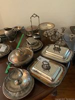 Overview of various silverplate serving dishes, candelabras, and trays on table.
