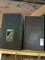 Two black rectangular ADS LS20 speakers on a wooden shelf, front and rear views shown, metal mesh grille on front, connection ports on rear.