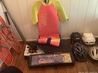 Photo showing pink and yellow O'Neill wetsuit, two croquet sets in cases, four helmets (two bike and two hockey helmets) on floor.