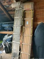 Two long wooden toboggans leaning against a wall in a garage. One with natural wood finish and Torpedo label, the other weathered gray with broken slat.