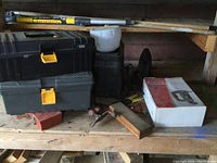 Wide view showing two black plastic toolboxes, Wagner electric sprayer, sanding poles, bar clamp, and hand tools on wooden shelf.