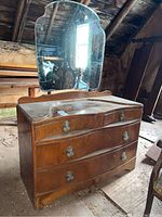 Front view of vintage wooden vanity dresser with attached scalloped mirror showing wood finish, ornate metal drawer handles, and surface wear.