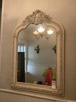 Full view of the large ornate wood framed wall mirror with reflective glass showing part of a chandelier and room interior