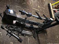 Photo of collapsed black and silver Thule bicycle carrier rack with padded bike supports and straps, viewed from above on a dark floor.