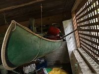 Green fiberglass canoe hanging indoors showing hull and wooden trim.
