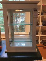 Front view of white wooden display cabinet with three glass shelves and an internal light fixture visible on top inside.