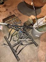Photo of metal bike rack with bungee cords, white bucket with fishing net handle visible, and other fishing equipment on basement floor.