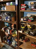 Two shelving units filled with assorted hardware boxes, various lightbulbs, and metal baskets in a basement setting