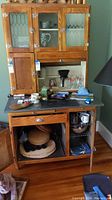 Front view of wood Hoosier cabinet with glass upper doors and black countertop surface, showing scratches and some contents removed.