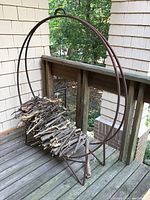 Metal log holder with round frame placed on wooden deck, loaded with small sticks for display.