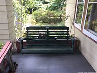 Front view of dark green wooden porch swing hanging from chains on a porch.