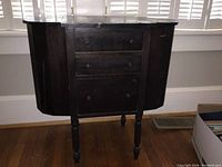 Front view of vintage wooden sewing table showing three drawers and hinged side leaves.