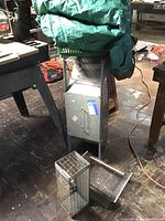 Green tarp folded atop a large metallic box with three metal live animal traps of different sizes on the floor around the box.