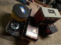Top perspective of bucket seat, multiple toolboxes, hardware organizers and rolls of tape on basement floor