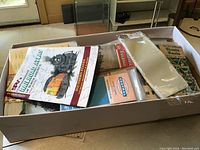Top view of a box filled with vintage railroad maps, booklets, and timetables, some in plastic sleeves.