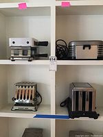 Three vintage toasters arranged on white shelving, showing different designs including Westinghouse branded toaster and others with chrome finishes and black handles.